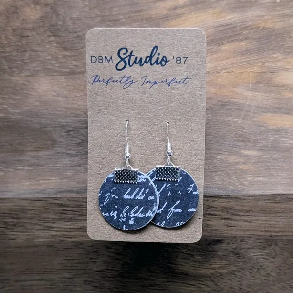 uarter size round earrings made from layers of paper modpodged together, black with white cursive front and plain black back. The color of the sides made by the paper inside is black. Silver-tone findings.